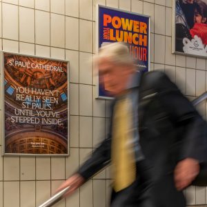 Blurred commuter walking past an A4 St Paul's ad poster on the london tube