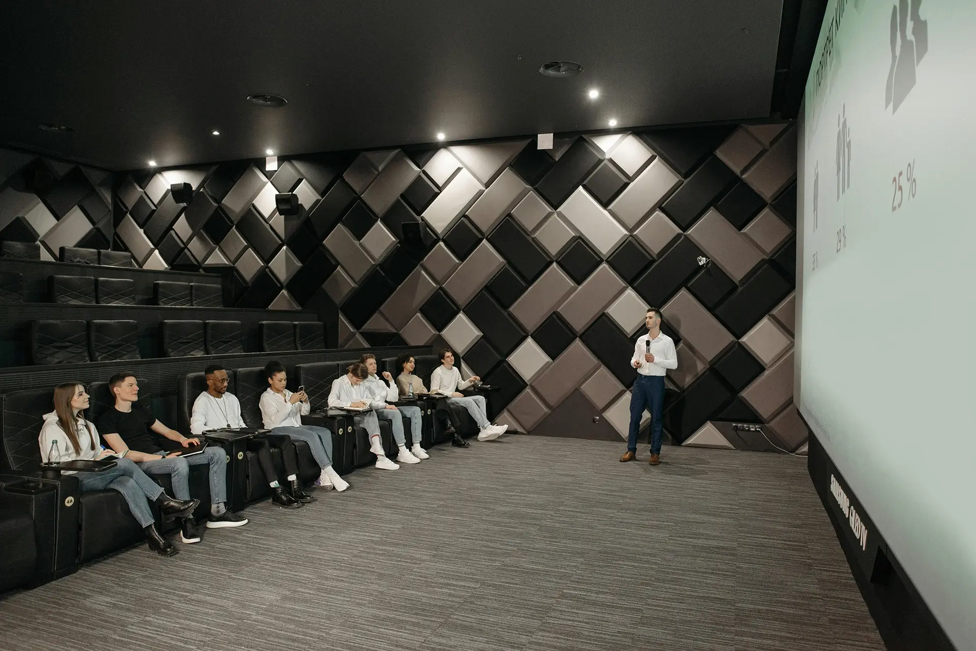 A cinema style room with people taking notes during a presentation