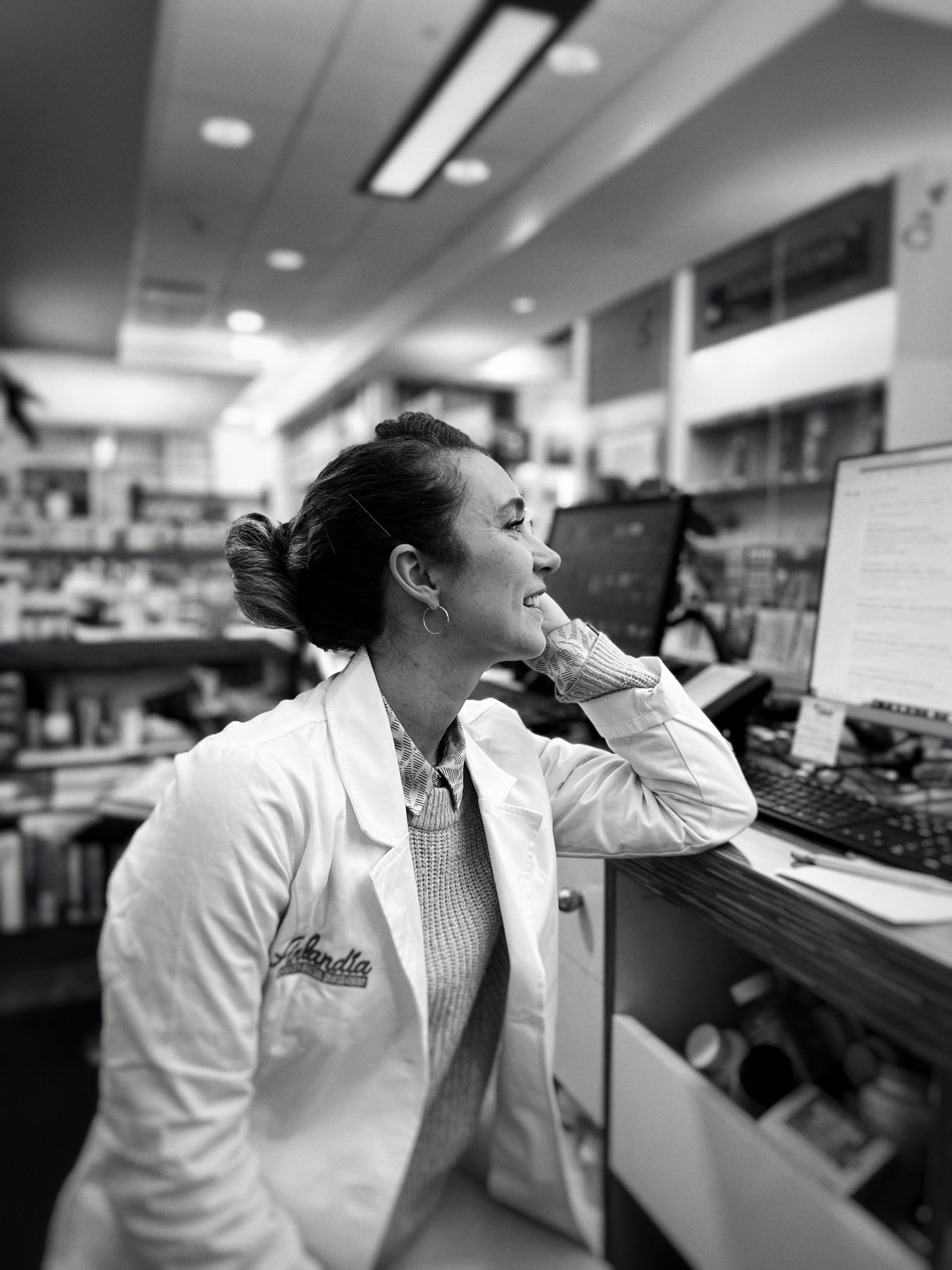 black and white photo of a female pahrmacist in a pharmacy sat in front of a computer